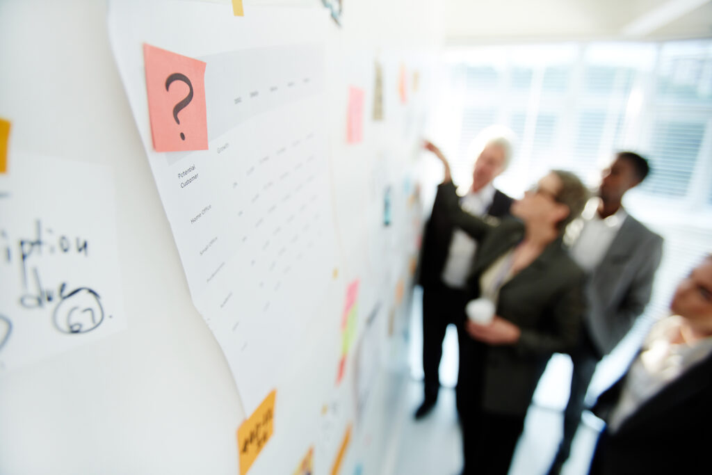 Multi-ethnic team of talented white collar workers gathered together at marker board while having joint project discussion at spacious open plan office, focus on foreground